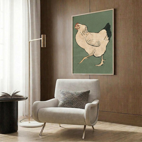 May include: Vintage Japanese woodblock print of a cream-colored hen with black tail feathers on sage green background, displayed in light wooden frame on wood-paneled wall above beige upholstered armchair with geometric patterned pillow, brass floor lamp and side table with open book nearby