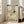 May include: Vintage 1910 children's book illustration poster in light wood frame, leaning against white wall near beige upholstered chair. Art shows sleeping child in bed with small red-dressed fairies climbing curtain cords and playing nearby. Soft earth tones with decorative border featuring oval motifs. Natural lighting from windows creates warm, cozy nursery atmosphere.