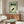 May include: Japanese poster print with green background featuring black goldfish character surrounded by cream-colored swirls, displayed above wooden mid-century modern credenza in minimalist living room with white curved chair, glass coffee table, and warm natural lighting
