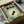 May include: Framed vintage-style Japanese poster with green background featuring black silhouette goldfish in center of cream ripple circles, Japanese text at top, small character illustration at bottom, displayed in wooden box with tissue paper wrapping and wooden dowels on sides