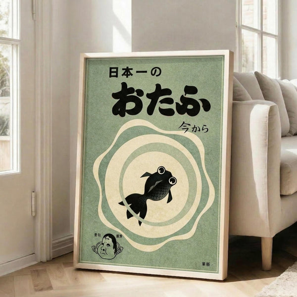 May include: Framed vintage-style Japanese poster with sage green background featuring black goldfish in cream circular ripples, Japanese text at top, small character illustration in bottom corner, displayed on wooden floor next to beige upholstered chair in bright room with white walls and windows.