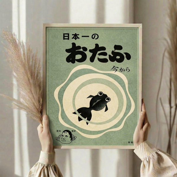 May include: A person in a cream ruffled blouse holds a framed vintage-style Japanese poster featuring a black goldfish in concentric cream and green circles on sage green background with Japanese text. They hold dried wheat stems in their other hand against white curtained windows.