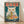 May include: Framed poster print featuring a white cat with golden eyes eating ramen noodles from a dark bowl. The cat holds chopsticks with noodles streaming from its mouth. Red Japanese characters appear at the top against a teal background. The bowl contains eggs, meat, and greens. Vintage-style artwork in wood frame, displayed on light wooden floor against white wall with soft lighting creating diagonal shadows.
