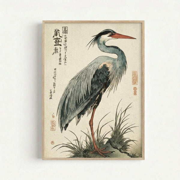Vintage Japanese woodblock print featuring a grey heron with long orange beak and elegant plumage standing among marsh grasses. The bird is rendered in muted blue-grey tones against a cream background, with Japanese calligraphy and red seals visible. The artwork is displayed in a simple light wood frame on a white wall, showing the delicate line work and traditional ukiyo-e artistic style.