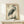 May include: Japanese woodblock print of a grey heron with long orange beak and legs standing among marsh grasses, featuring traditional calligraphy and red stamps, displayed in light wooden frame on pale wood console table next to small white wrapped gift box against cream wall