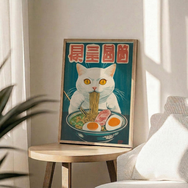 May include: Framed poster print featuring a white cat with golden eyes eating ramen noodles from a blue bowl, with red Japanese characters above on teal background. Displayed on light wood round side table next to beige upholstered chair with throw pillow. Natural sunlight streams through window, casting shadows from nearby plant leaves onto white wall.