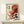 May include: Framed Japanese-style artwork featuring a large red octopus with flowing tentacles emerging from ocean waves, combining traditional ukiyo-e wave motifs with bold red coloring against cream background. Black Japanese text appears in upper left corner. Print displayed on light wood shelf against white wall with small white geometric objects nearby.