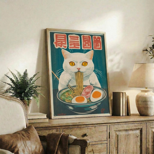 May include: Framed poster featuring a white cat with yellow eyes eating ramen noodles from a blue bowl, with red Japanese characters on teal background, displayed on rustic wooden sideboard alongside books, ceramic vase, and fern plant in cozy living room setting with beige armchair visible.