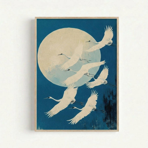 May include: Framed vintage Japanese woodblock print showing white cranes flying against deep blue night sky with large pale yellow full moon. The birds have outstretched wings and long necks, rendered in cream and white tones. Light wooden frame hangs on white wall, casting subtle shadow. Art style features traditional Asian aesthetic with bold color contrast and graceful bird silhouettes.