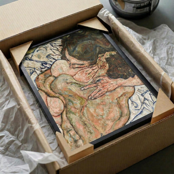 May include: Framed reproduction of an expressionist artwork showing two embracing nude figures in muted earth tones of pink, green and brown, with flowing organic forms and visible brushwork. The black-framed print sits in an open cardboard shipping box with white tissue paper and wooden dowels, photographed on a white surface with dramatic lighting.