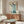 May include: Chinese-style artwork featuring five blue cranes with long necks and dark beaks against cream background with black calligraphy text, displayed in thin wood frame above walnut credenza. Modern living room setting with white curved chair, brass floor lamp, oval glass coffee table, and neutral walls.
