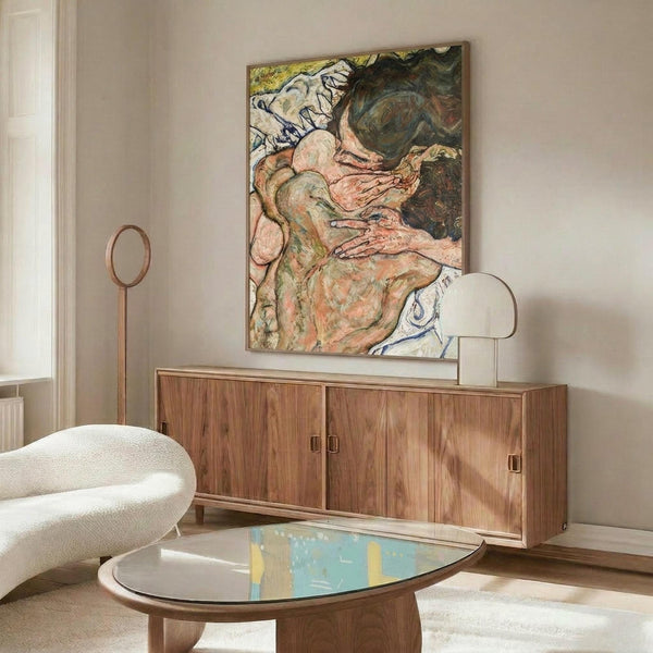 May include: Expressionist artwork in warm earth tones depicting embracing figures, displayed above a mid-century walnut credenza in a modern living room. The painting features flowing, organic forms in pink, green, and cream hues with bold brushstrokes. White sculptural chair and oval glass coffee table complete the contemporary interior setting with neutral walls and natural lighting.