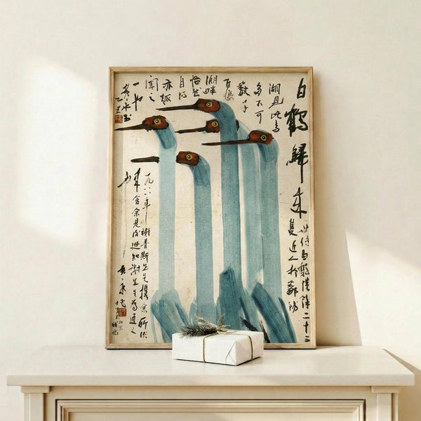 May include: Framed vintage Chinese artwork featuring five stylized cranes with long blue-green necks, brown heads, and black beaks against cream background with black calligraphy text. Light wood frame displayed on pale wooden console table with small white wrapped gift box. Minimalist setting with white wall backdrop.