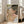 May include: Framed reproduction of an expressionist painting showing two embracing nude figures rendered in earthy tones of pink, green, and brown with bold black outlines. The artwork is displayed in a light wood frame leaning against a beige armchair in a bright living room with white walls and large windows.