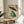 May include: Framed Japanese woodblock-style print featuring a green frog holding a bamboo umbrella in the rain, displayed on a round wooden side table next to a beige upholstered chair. The artwork shows traditional ukiyo-e aesthetic with vertical rain lines, red Japanese text cartouche, and muted earth tones in a light wood frame.