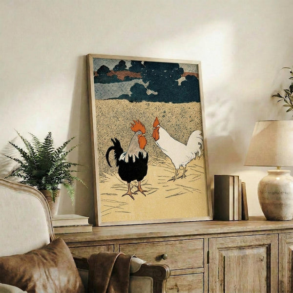 May include: Framed vintage-style poster featuring two roosters - one black with red crest, one white with red crest - on sandy ground beneath stormy blue-gray clouds. The artwork has a textured, woodblock print appearance with muted earth tones. Displayed on rustic wooden sideboard alongside fern plant, books, and ceramic vase in neutral-toned living room setting.