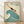 May include: Vintage-style travel poster in light wood frame leaning against white wall on wooden floor. Features art deco illustration of swimmer diving over stylized teal wave on cream background. Text reads "The Seaside Calls" and "Go By Train" with Kodak branding. Poster has weathered, aged appearance with muted teal and orange colors in retro tourism advertisement style.