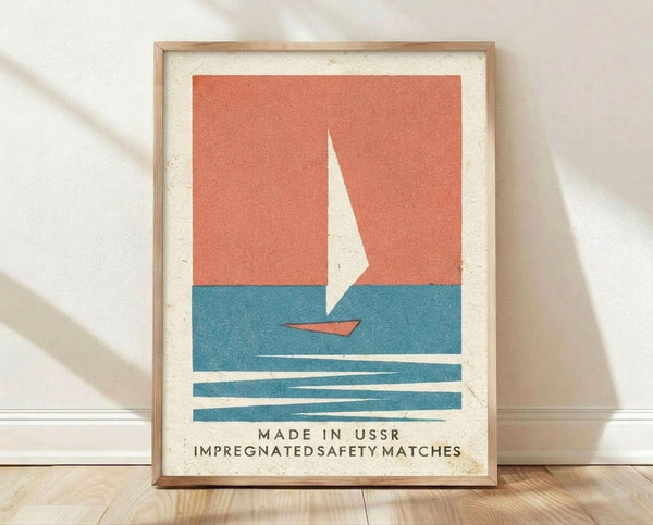 May include: Framed vintage-style poster print featuring minimalist sailboat illustration with white sail on coral orange sky and teal blue water, displayed in light wood frame against white wall on wooden floor with natural lighting and soft shadows