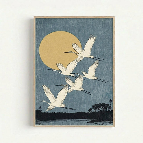 A framed vintage Japanese woodblock print showing five white cranes with outstretched wings flying across a blue-gray sky. A large golden moon sits in the upper left, while a dark silhouetted landscape with trees and water stretches across the bottom. The artwork has a textured, traditional printmaking appearance and is displayed in a simple light wood frame against a white wall.