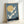 May include: A framed vintage Japanese woodblock print showing six white cranes flying diagonally across a blue sky with a large golden moon. The birds have detailed feathers and long necks, soaring above a dark silhouetted landscape with trees and water. The artwork is displayed in a light wood frame, leaning against a white wall on a white surface, showcasing the traditional ukiyo-e art style with muted blue, cream, and black tones.