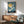 May include: Vintage Japanese woodblock print showing white cranes flying against blue sky with golden moon, displayed in wooden frame above mid-century modern credenza and sage green armchair in sunlit living room setting