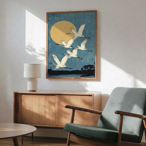 May include: Vintage Japanese woodblock print showing white cranes flying against blue sky with golden moon, displayed in wooden frame above mid-century modern credenza and sage green armchair in sunlit living room setting
