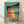 May include: Framed vintage-style poster with turquoise background showing five women in colorful dresses dancing in a line - red, orange, yellow, green, and blue outfits. Text reads "Dance more" in orange lettering. The illustration has a retro mid-century modern art style with geometric shapes and bold colors. Light wooden frame sits on hardwood flooring against white wall with natural lighting and shadows visible.