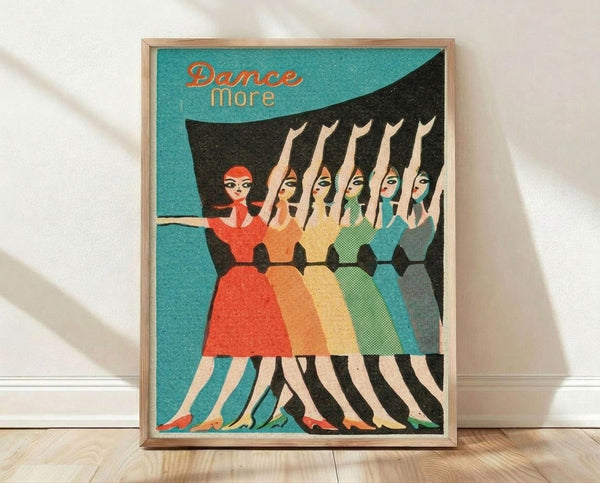 May include: Framed vintage-style poster with turquoise background showing five women in colorful dresses dancing in a line - red, orange, yellow, green, and blue outfits. Text reads "Dance more" in orange lettering. The illustration has a retro mid-century modern art style with geometric shapes and bold colors. Light wooden frame sits on hardwood flooring against white wall with natural lighting and shadows visible.