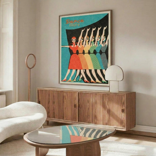 May include: Vintage-style poster with turquoise background showing five women in colorful dresses - red, orange, yellow, green, and blue - dancing in a line with arms raised. Text reads "Dance More" in orange lettering. Poster is framed in light wood and displayed above a mid-century modern walnut credenza in a bright living room with white curved chair, glass coffee table, and white table lamp.
