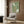 May include: Green vintage-style poster with white squid and abalone illustrations alongside Japanese text, displayed in wooden frame on wood-paneled wall above beige upholstered armchair with geometric patterned pillow, brass floor lamp and dark round side table with open book nearby