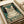 May include: Vintage-style poster print featuring a tabby cat wearing black headphones on a teal green background with musical notes. Text reads "MUSIC" at top and "BECAUSE MURDER IS WRONG" at bottom in distressed cream lettering. Print shown on white paper with rolled paper tubes nearby on light wooden surface.
