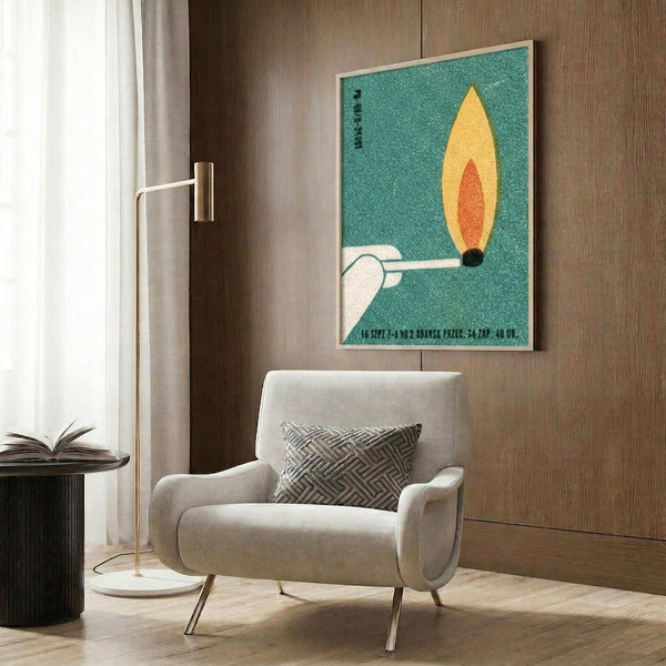 May include: Vintage-style poster with turquoise background featuring stylized matchstick with yellow and orange flame, mounted in light wood frame on dark wood paneled wall above beige upholstered armchair with geometric patterned pillow, brass floor lamp and side table with open book visible in modern living room setting