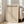 May include: Framed beige poster with black text reading "BAUHAUS" and "LESS IS MORE" above a vertical row of triangular shapes, displayed on wooden floor against white wall next to beige upholstered sofa in bright, naturally-lit room with large windows.