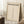 May include: Bauhaus-style minimalist poster in light wood frame leaning against white wainscoted wall. Cream background with bold black text reading "BAUHAUS" and "LESS IS MORE" above vertical row of geometric triangles. German exhibition text at bottom. Shown with coffee cup on wooden block and cozy beige throw blanket on white textured rug.