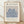 May include: Framed art print featuring blue botanical cutout shapes on beige background, displayed in light wood frame against white textured wall on wooden floor with natural lighting and shadows