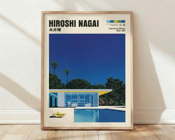 May include: Framed poster print leaning against white wall on light wooden floor. Shows modernist poolside scene with white and yellow mid-century house, bright blue swimming pool, palm trees, and deep blue sky. Yellow lounge chairs beside pool. Cream matting in natural wood frame. Japanese text and "Pacific Breeze Collection Tokyo, 1982" at top with colorful logo.