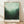 May include: Framed poster displaying misty forest landscape in green tones that fade from dark evergreen trees at bottom to pale mint sky at top. Text reads "MARK ROTHKO A RETROSPECTIVE 1949-1970 MUSEUM OF MODERN ART, NEW YORK CITY" in black letters on white bottom margin. Natural wood frame leans against white textured wall on light wooden floor with soft shadows.