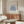May include: Framed Matisse exhibition poster with blue botanical cutout design displayed above mid-century walnut credenza in minimalist living room. White upholstered chair and glass coffee table visible. Poster features cream background with blue coral-like shapes and French gallery text. Natural lighting creates soft shadows on neutral walls.