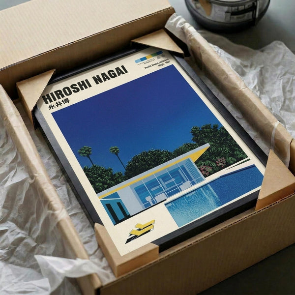 A framed art print featuring a modernist house with large glass windows beside a bright blue swimming pool, set against a deep blue sky with lush green trees. The architectural illustration shows clean lines and mid-century design in vibrant blues, yellows, and greens. The print is carefully packaged in a cardboard box with protective wrapping materials, showing the professional shipping presentation.
