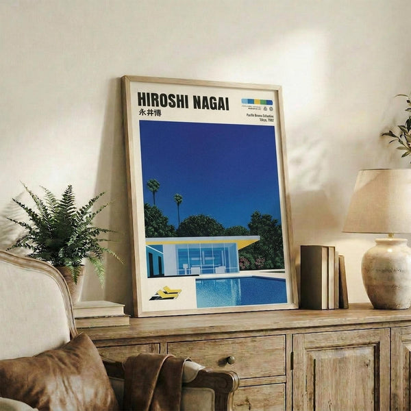 May include: Framed poster featuring a modernist house with swimming pool under bright blue sky with palm trees, displayed on rustic wooden sideboard alongside potted fern, ceramic vase, and stacked books in neutral-toned living room with beige upholstered furniture.