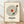 May include: Framed poster print featuring a vinyl record design with song lyrics arranged in concentric circles around a red center label and black tonearm. The cream-colored artwork displays placeholder text reading "SONG NAME," "ARTIST NAME," "YEAR," and "PERSONALIZED MESSAGE - OPTIONAL" in black typography. Light wood frame sits on wooden flooring against white textured wall with soft natural lighting and shadows.