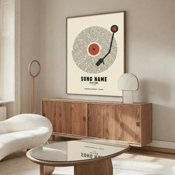 May include: Modern living room with beige walls featuring framed vinyl record poster art with red center label, black tonearm, and spiral text design. Wood credenza below holds white sculptural lamp. White curved chair and glass coffee table in foreground. Minimalist Scandinavian-style interior with warm wood tones and neutral palette.