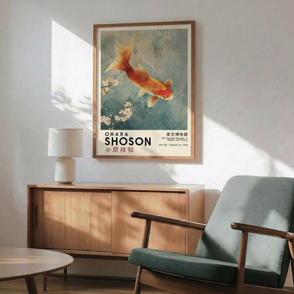 May include: A framed vintage Japanese art print featuring a golden-orange koi fish swimming among cherry blossoms in muted blue-green water. The poster hangs above a mid-century modern wood credenza with sliding doors, next to a ceramic table lamp. A teal upholstered armchair with wooden frame sits nearby on a round area rug. Natural sunlight creates geometric shadows on the white wall.