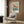 May include: Framed vintage Japanese art poster featuring an orange and red koi fish swimming among cherry blossoms on a blue-green background, displayed above a cream upholstered armchair with geometric pillow in a modern living room with wood panel walls, brass floor lamp, and dark round side table with open book.