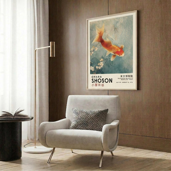 May include: Framed vintage Japanese art poster featuring an orange and red koi fish swimming among cherry blossoms on a blue-green background, displayed above a cream upholstered armchair with geometric pillow in a modern living room with wood panel walls, brass floor lamp, and dark round side table with open book.