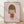 May include: Framed art print featuring a stylized cartoon girl with olive green bob haircut and closed eyes, wearing an orange-red dress, set against a soft pink background. The minimalist illustration shows the character with a small tongue sticking out. Light wooden frame sits on wooden flooring against white walls with natural window light creating gentle shadows.