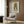 May include: Framed poster of anime-style girl with large golden blonde beehive hair and big dark eyes on light blue background, displayed on wood paneled wall above beige upholstered armchair with geometric patterned pillow, brass floor lamp and side table with open book visible in modern living room setting