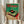 May include: Person holding framed vintage Japanese turntable poster with pampas grass stems. Green and red retro-style artwork shows detailed turntable illustration with Japanese text. Cream wooden frame against white curtains and neutral clothing create minimalist styling scene.