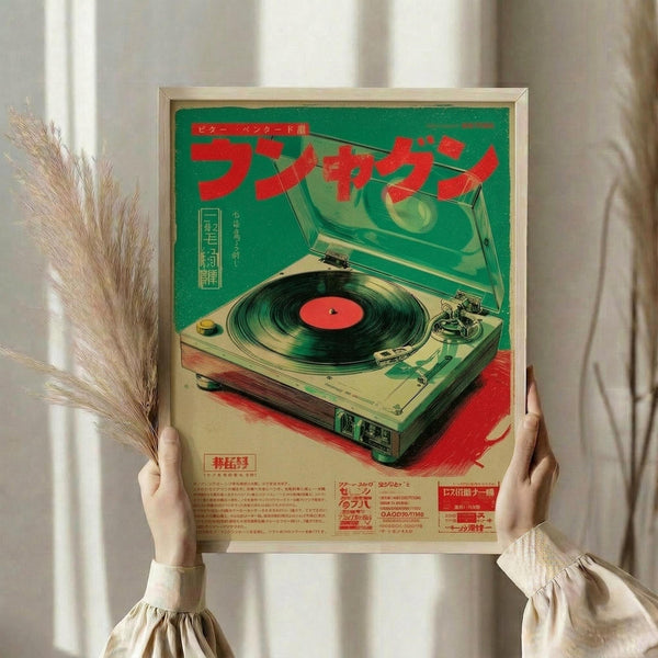 May include: Person holding framed vintage Japanese turntable poster with pampas grass stems. Green and red retro-style artwork shows detailed turntable illustration with Japanese text. Cream wooden frame against white curtains and neutral clothing create minimalist styling scene.