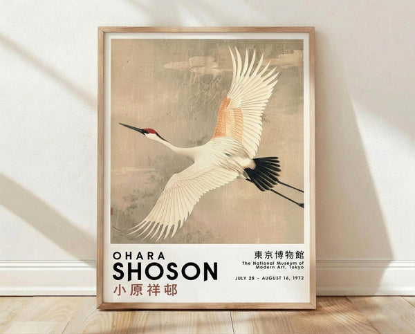 May include: Framed vintage Japanese art print showing a white crane with red crown and black wing tips flying through cloudy sky, displayed in light wood frame against white textured wall on wooden floor. Poster features museum exhibition text for Ohara Shoson at Tokyo National Museum from 1972. Natural lighting creates soft shadows across the minimalist room setting.